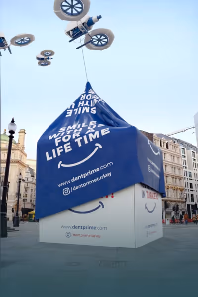 Dronlar tarafından büyük bir kutunun üzerini örtülen mavi kumaş, üzerinde Dentprime web sitesi ve Instagram adresi ile 'Smile with us for a lifetime' yazısı var.