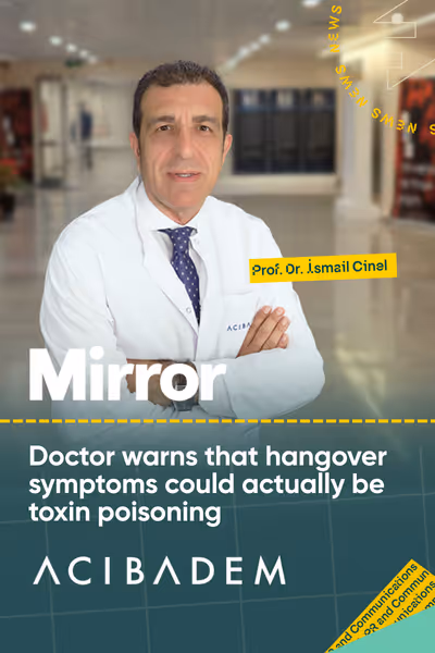 Prof. Dr. İsmail Cinel beyaz önlük ve kravat giymiş, kolları çaprazlı kapalı, hastane koridorunda duruyor.