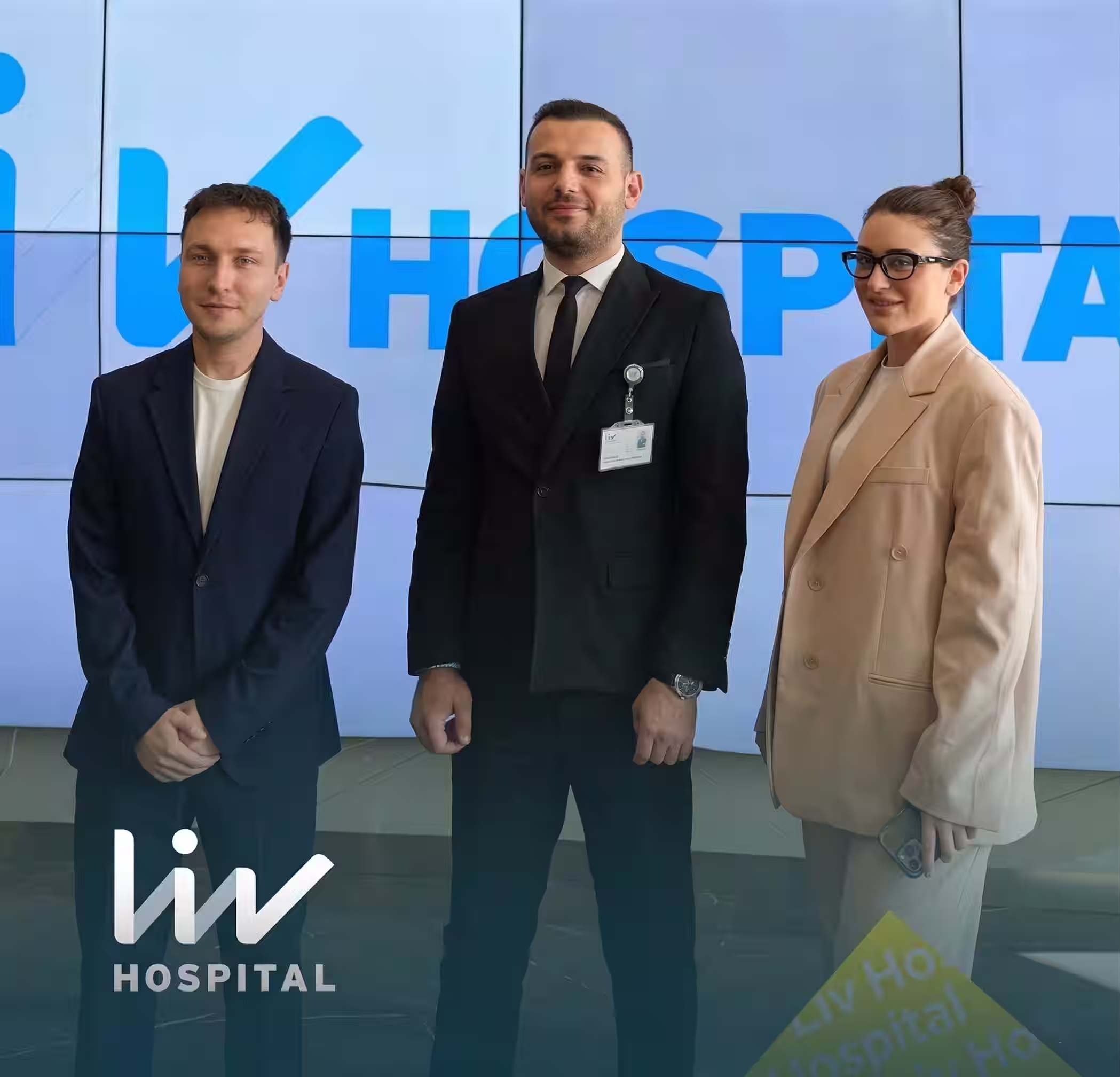 LIV Hospital logosu önünde takım elbise giymiş üç profesyonel kişi ayakta duruyor.
