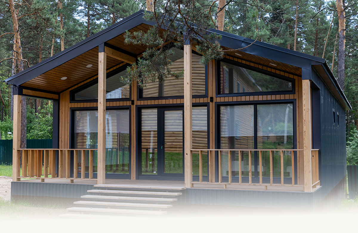 Modern wooden chalet with large glass windows and a porch surrounded by pine trees.