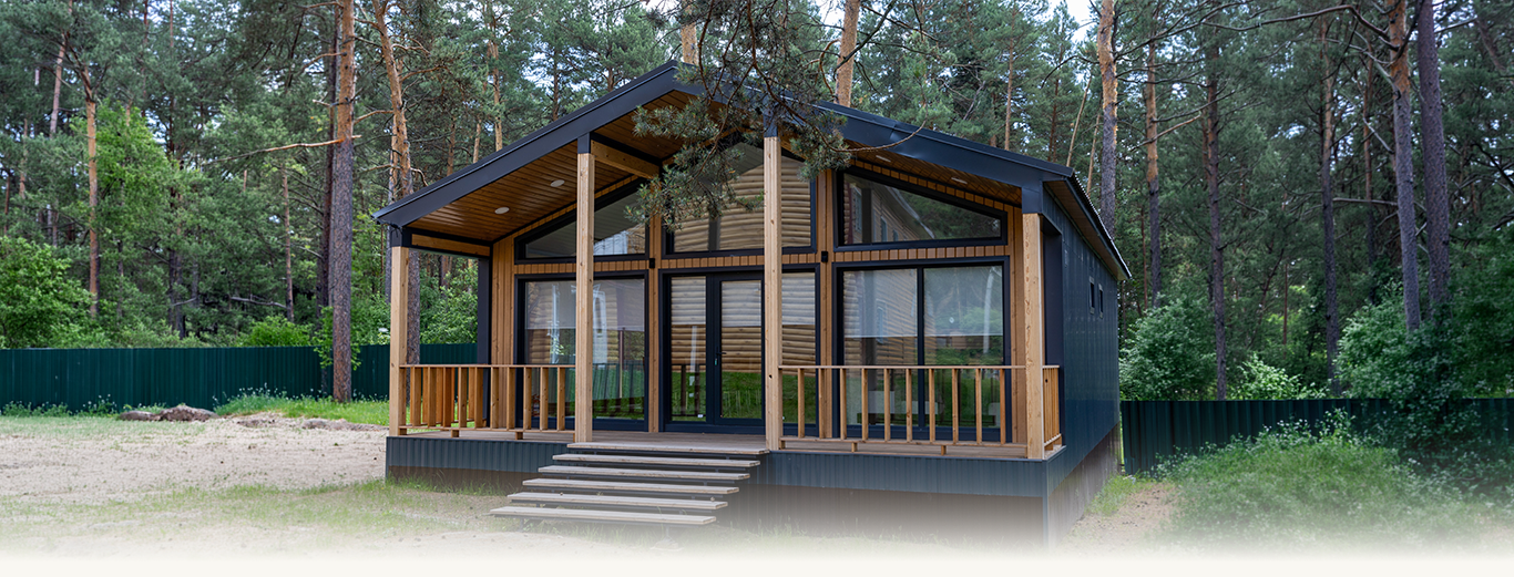 Modern wooden chalet with large glass windows and a porch surrounded by pine trees.