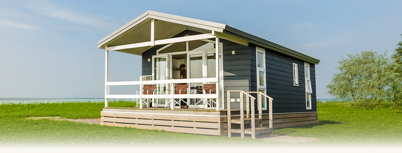 Modern dark gray cabin with porch, chairs, and person standing inside near open doors.