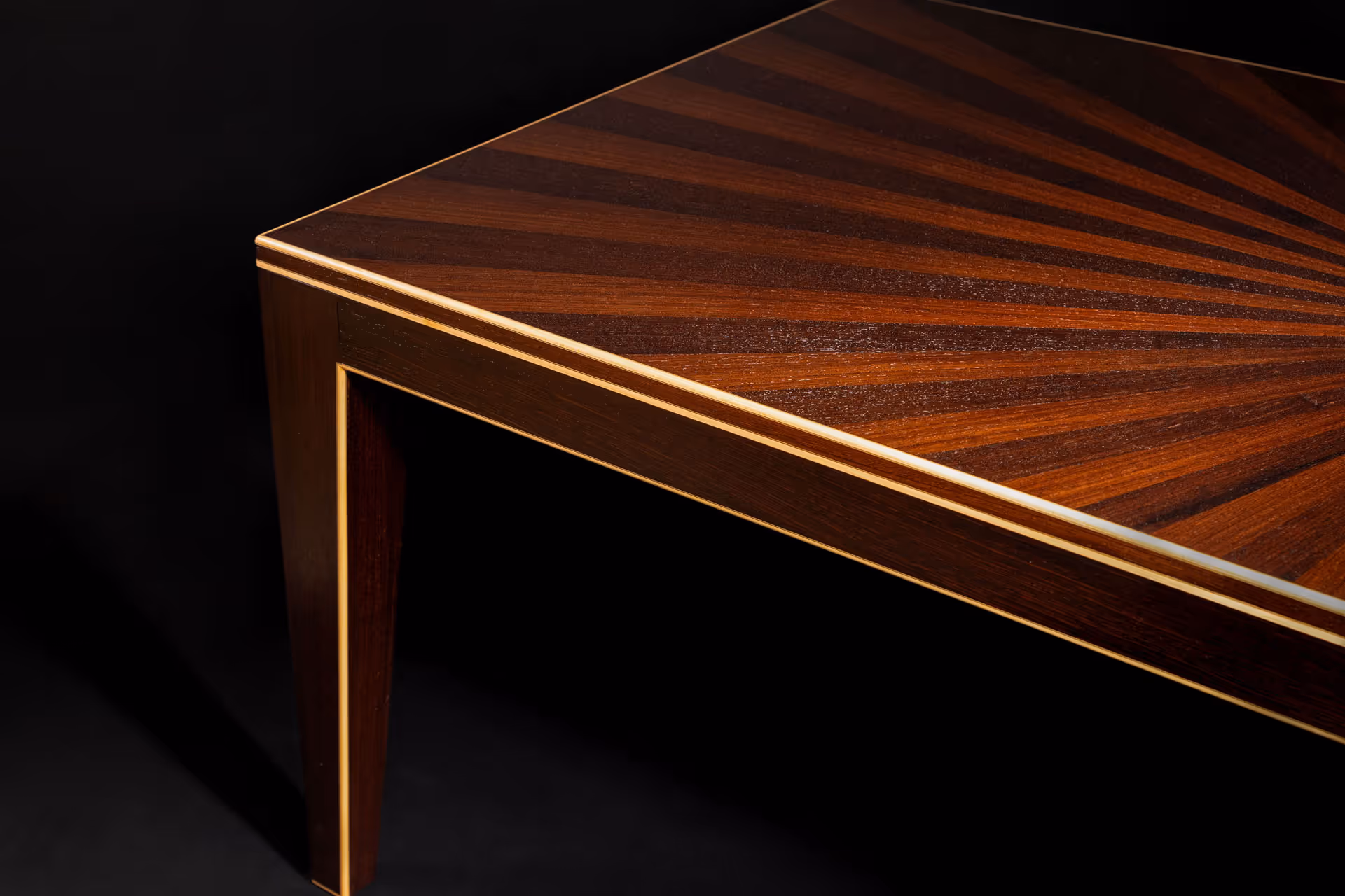 Close-up of a wooden table corner with a sunburst pattern and light trim on the edges.