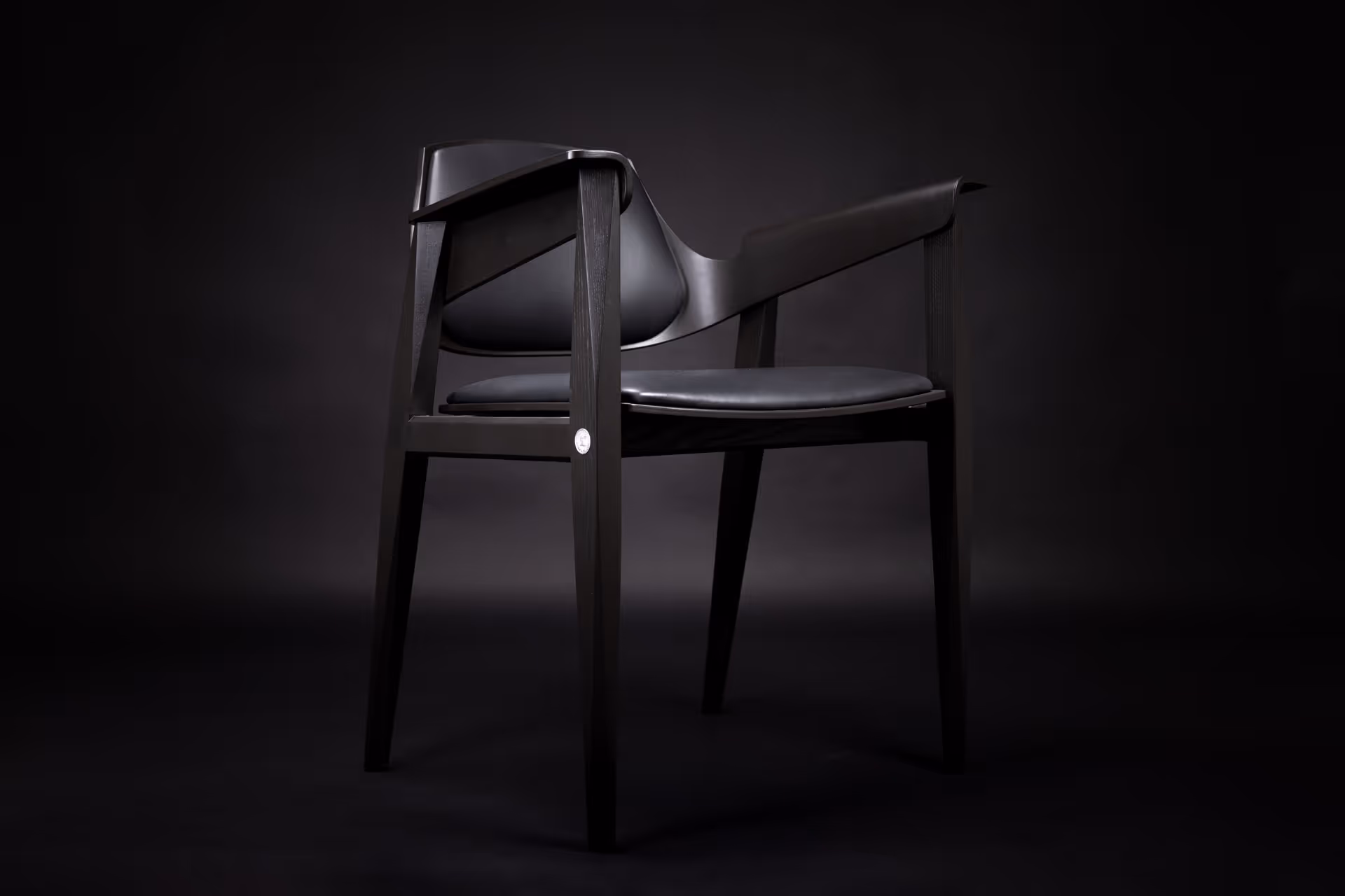 Modern black wooden chair with a sleek curved backrest and armrests on a black background.