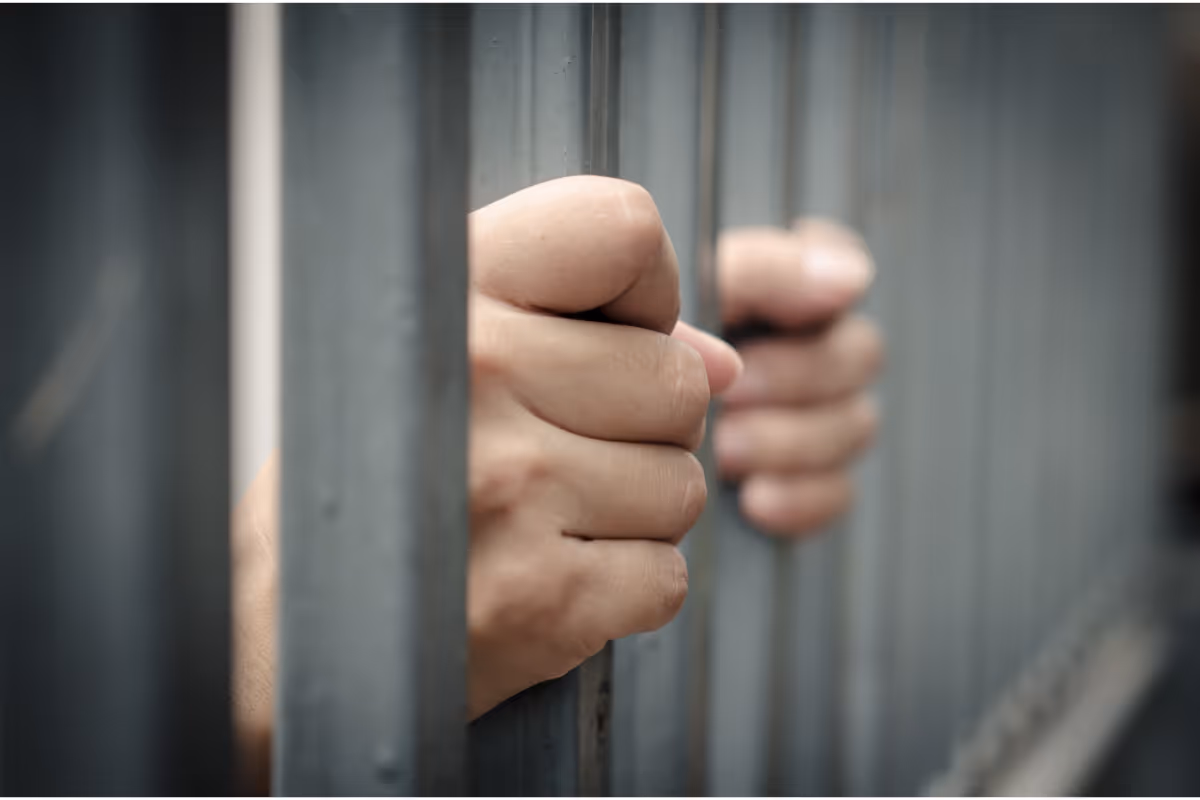 A person in jail with hands on the jail bars.