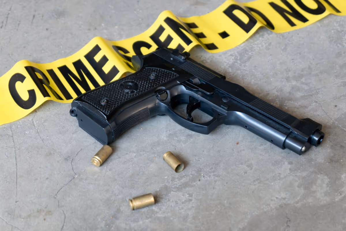 A gun on the floor with three bullet shells and caution tape.