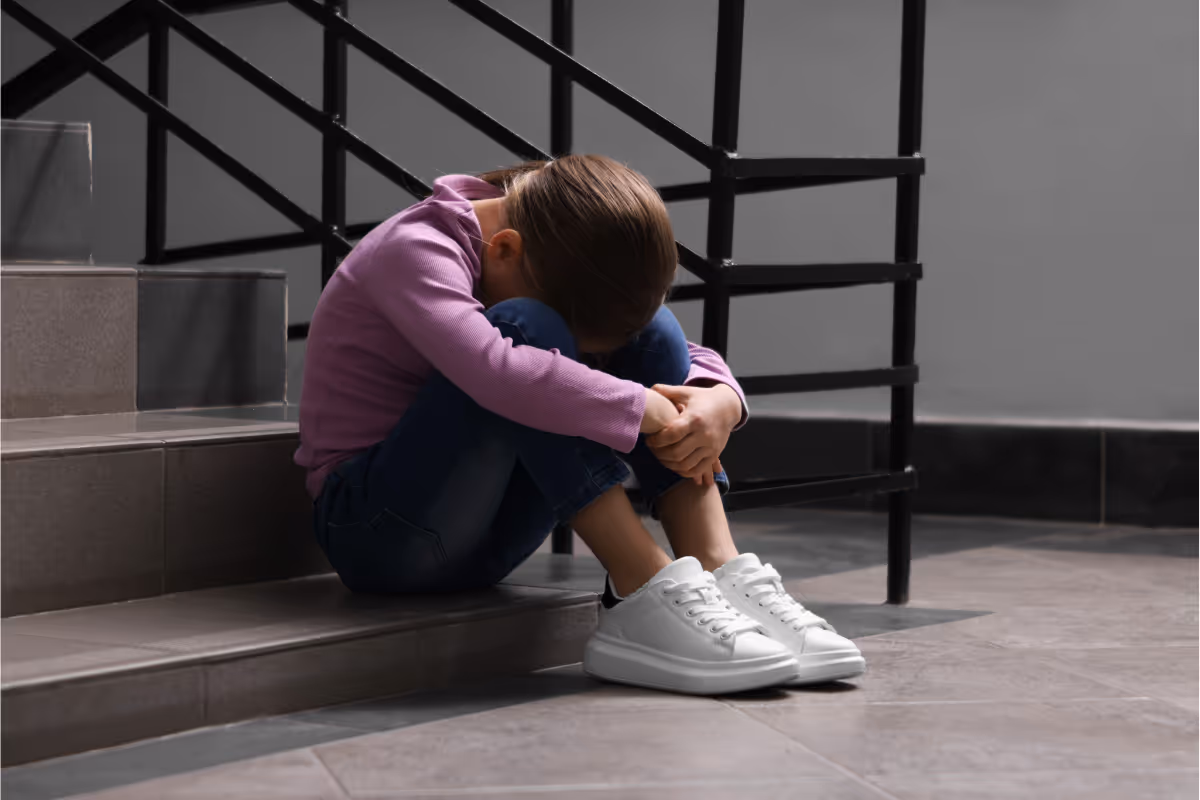 A child sitting on a staircase sad with their head on their knees.