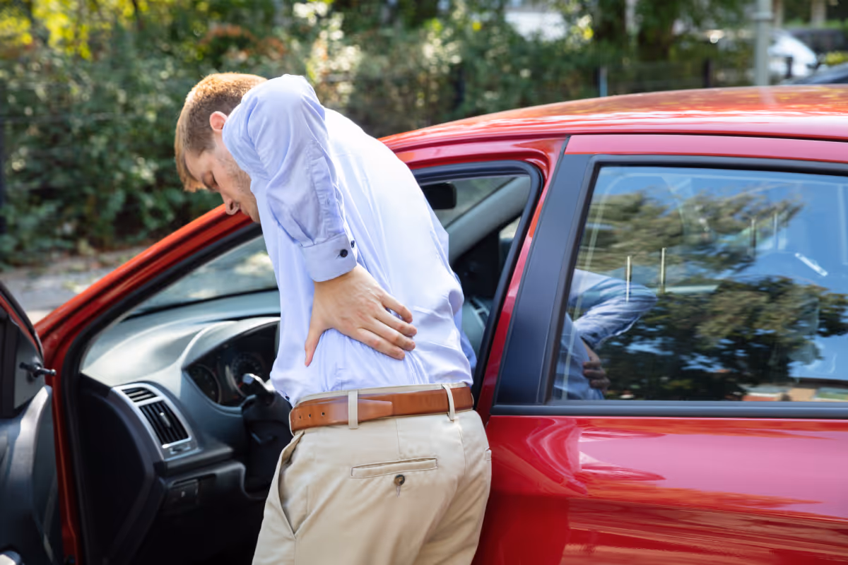 An older man holding his back after a car accident.