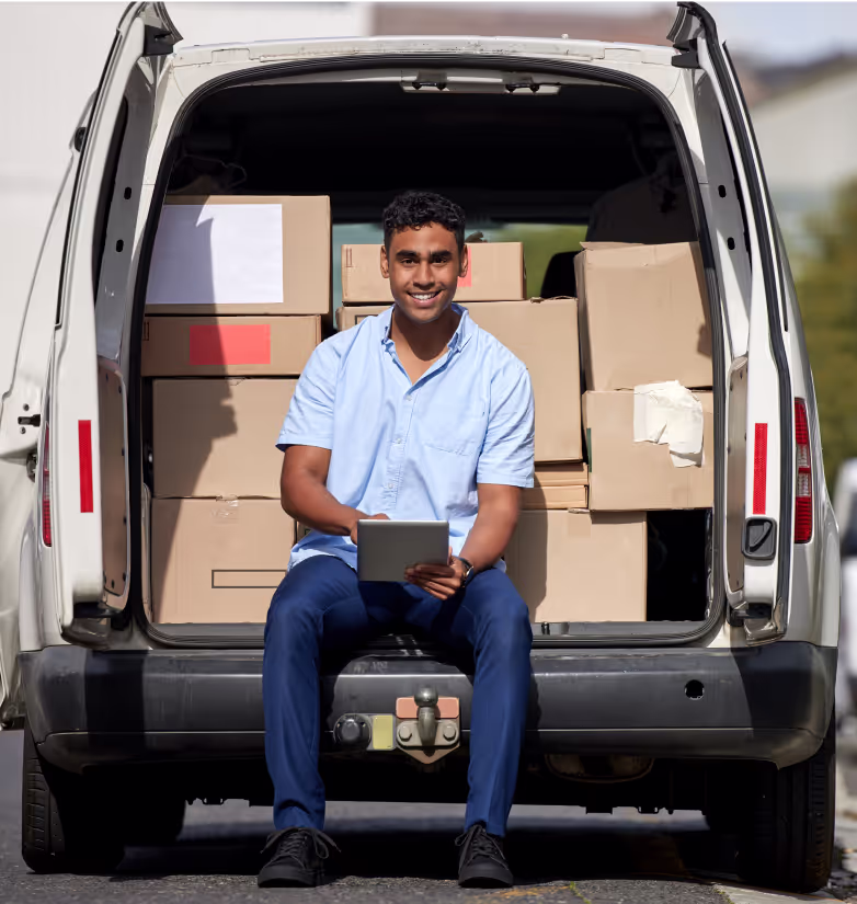 A delivery driver sitting at the back of his van, working on a tablet.