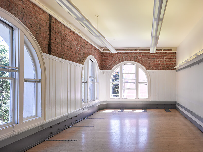 Empty Room A with large arched windows and hardwood floor, ready for various setups.