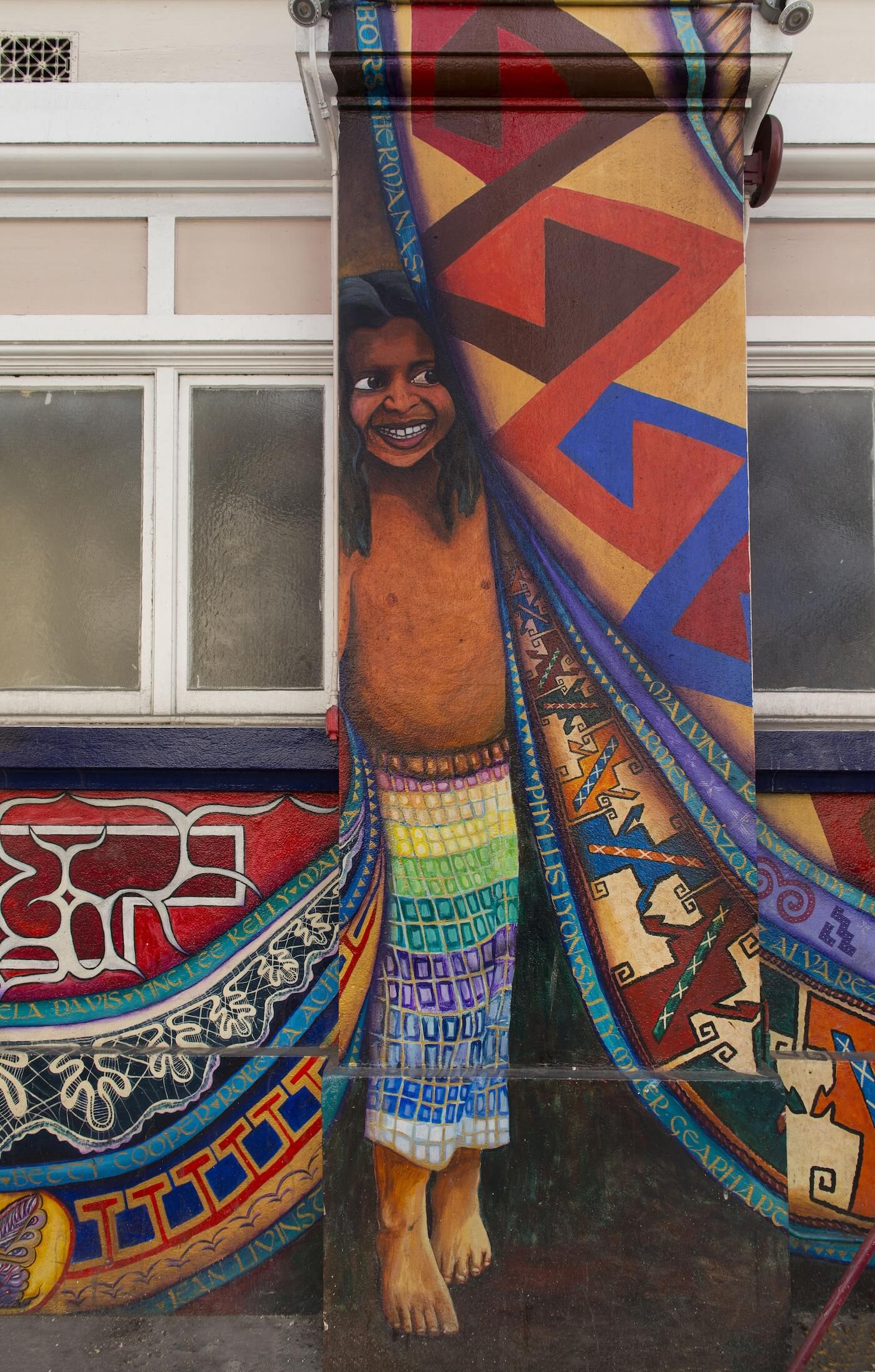 Depiction of a smiling Sri Lankan girl peeking out from behind a colorful mural curtain.