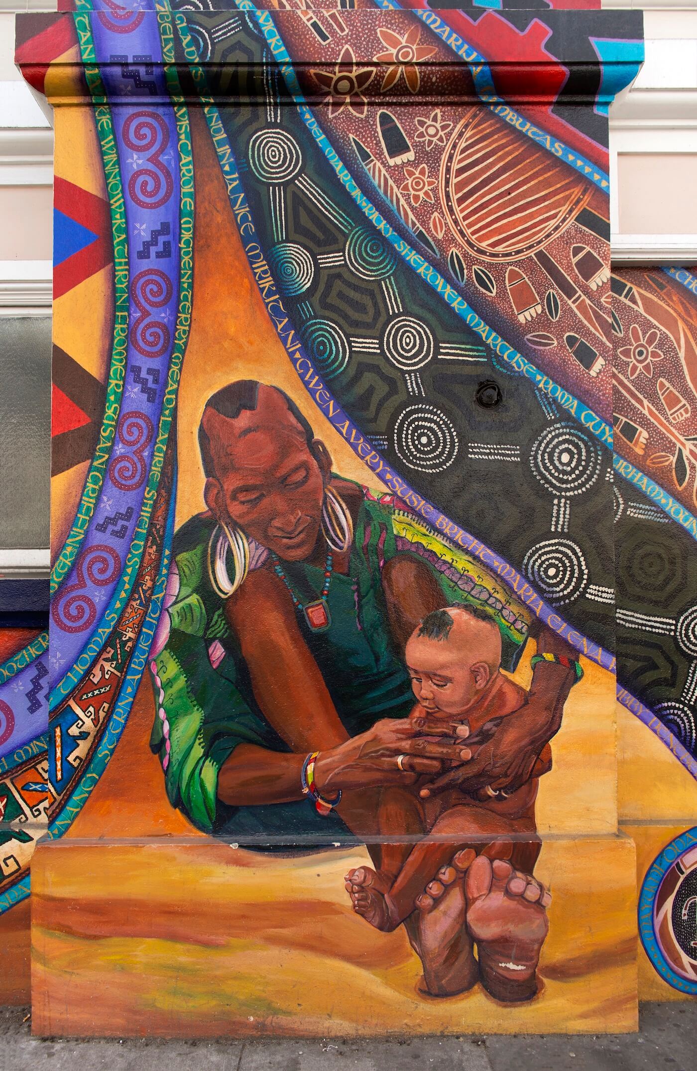 Wodaabe grandmother cradling a baby with intricate textile patterns surrounding them.