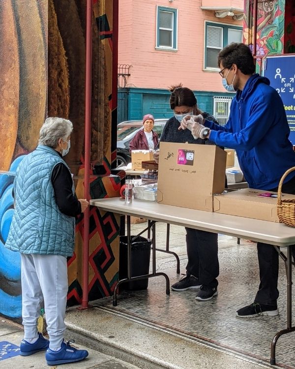 Volunteers distribute food boxes to a community member outside The Women’s Building as part of direct support programs.