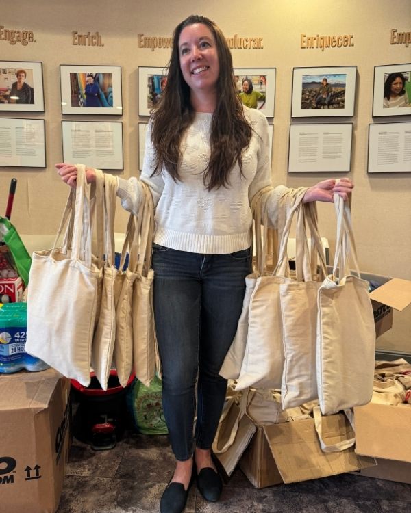 A woman holds multiple canvas tote bags prepared for community distribution as part of The Women’s Building’s giving programs.