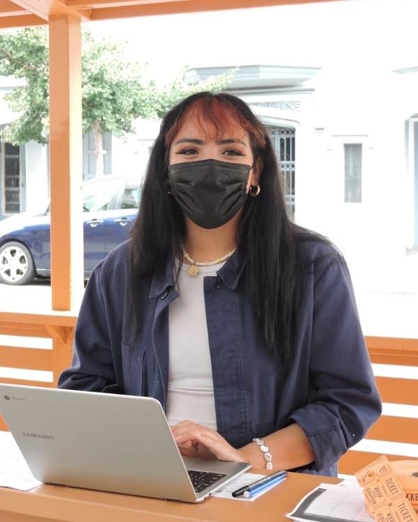 A masked volunteer at an outdoor table, working on a laptop during a community event.
