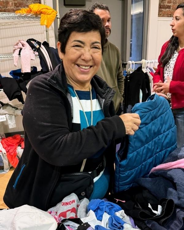 A cheerful volunteer organizing jackets and clothing donations during a community giveaway.