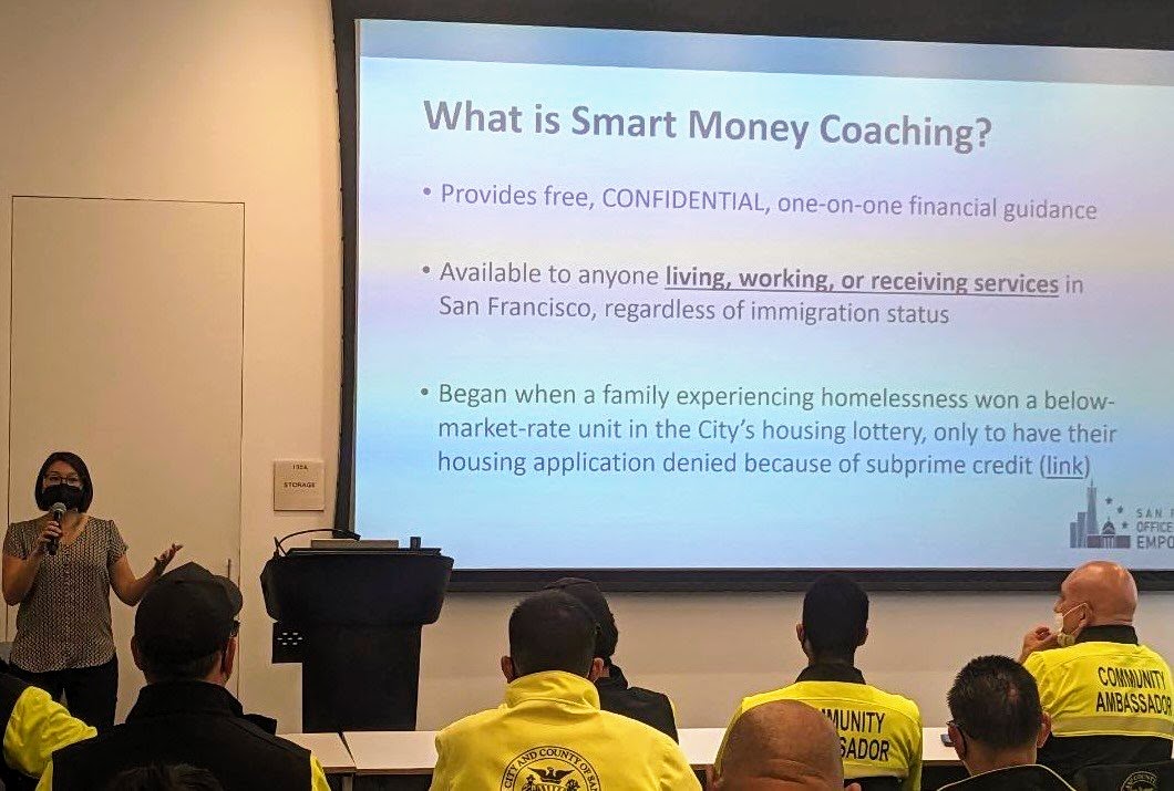 A presenter speaks to a group of Community Ambassadors in yellow uniforms about Smart Money Coaching, a free and confidential financial guidance program available to all San Francisco residents regardless of immigration status.