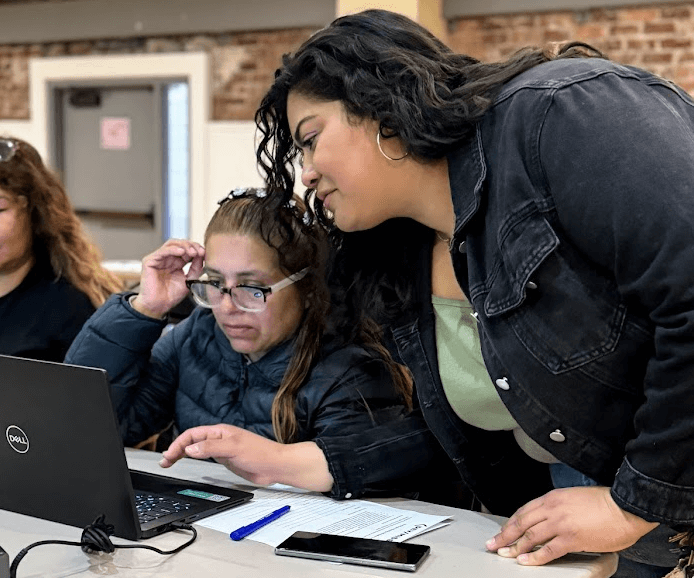 A Mobile Lab team member provides one-on-one digital support to a woman using a laptop during a hands-on community workshop.