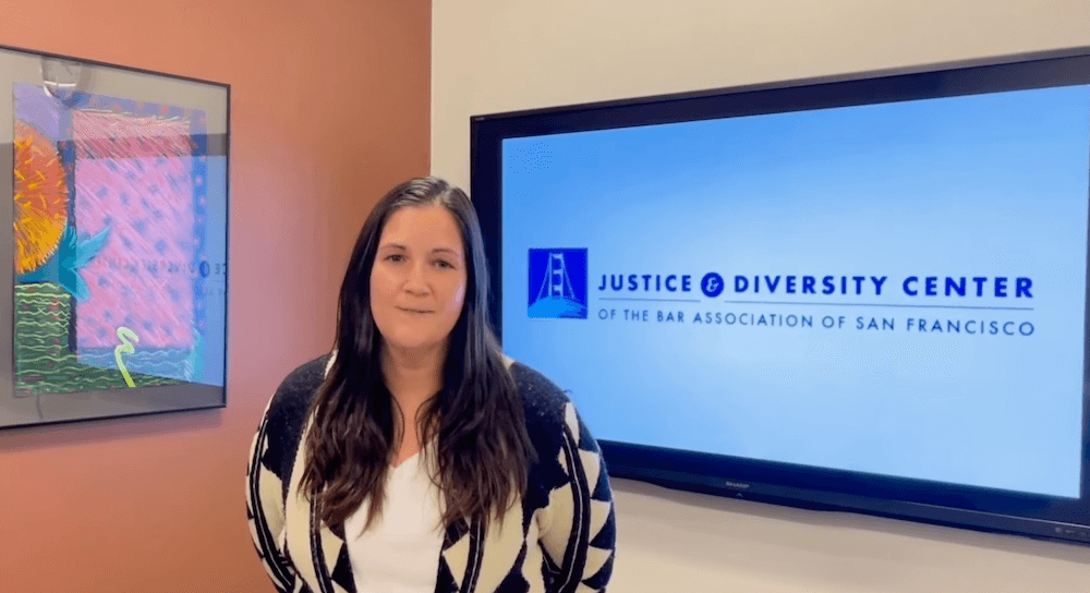 Representative from the Justice & Diversity Center of the Bar Association of San Francisco standing beside a screen displaying the organization's name and logo.