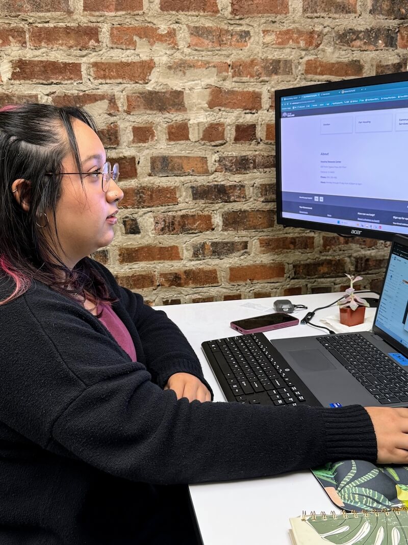 A staff member leans in to assist a participant with online forms, both focused on a laptop screen during a Post-Release Services session.