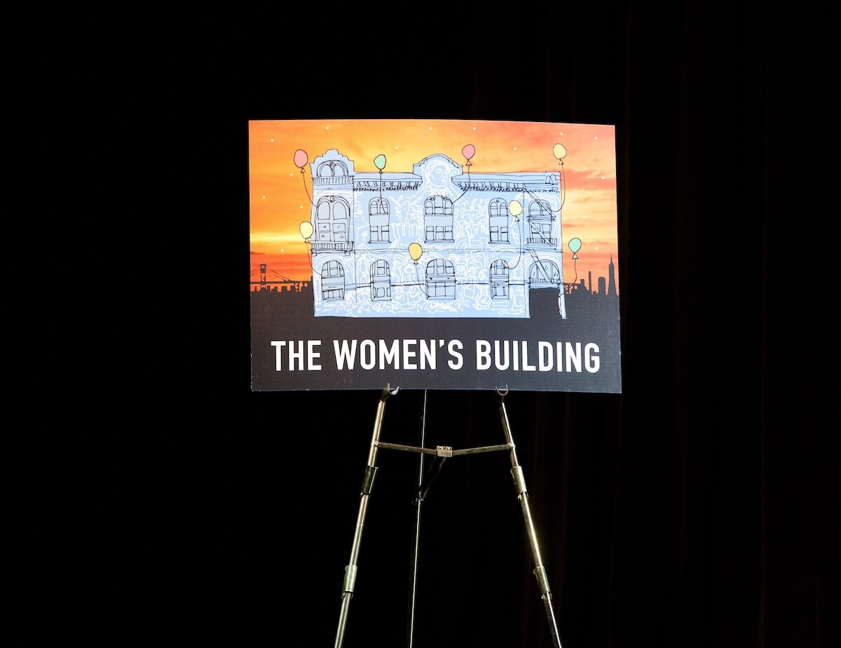 A colorful illustrated poster of The Women’s Building displayed on an easel against a black backdrop.