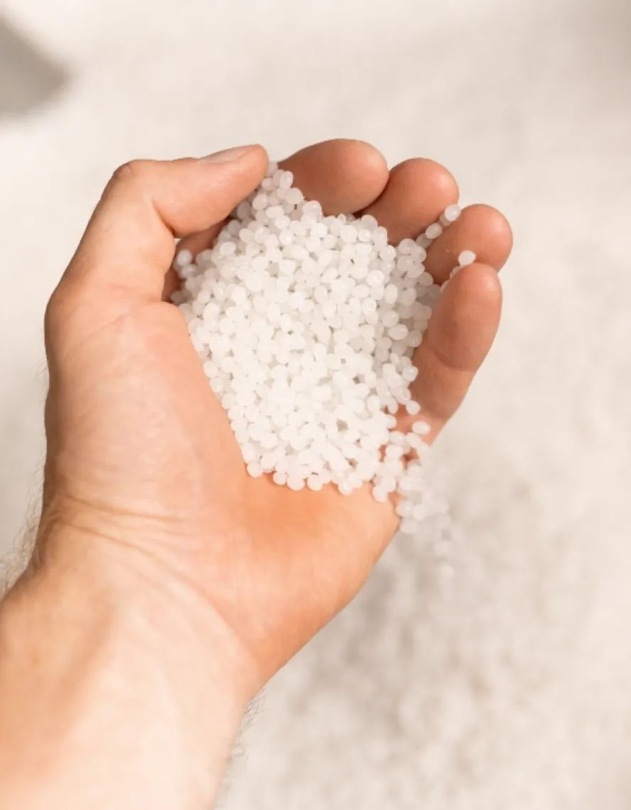 A hand holding white plastic pellets
