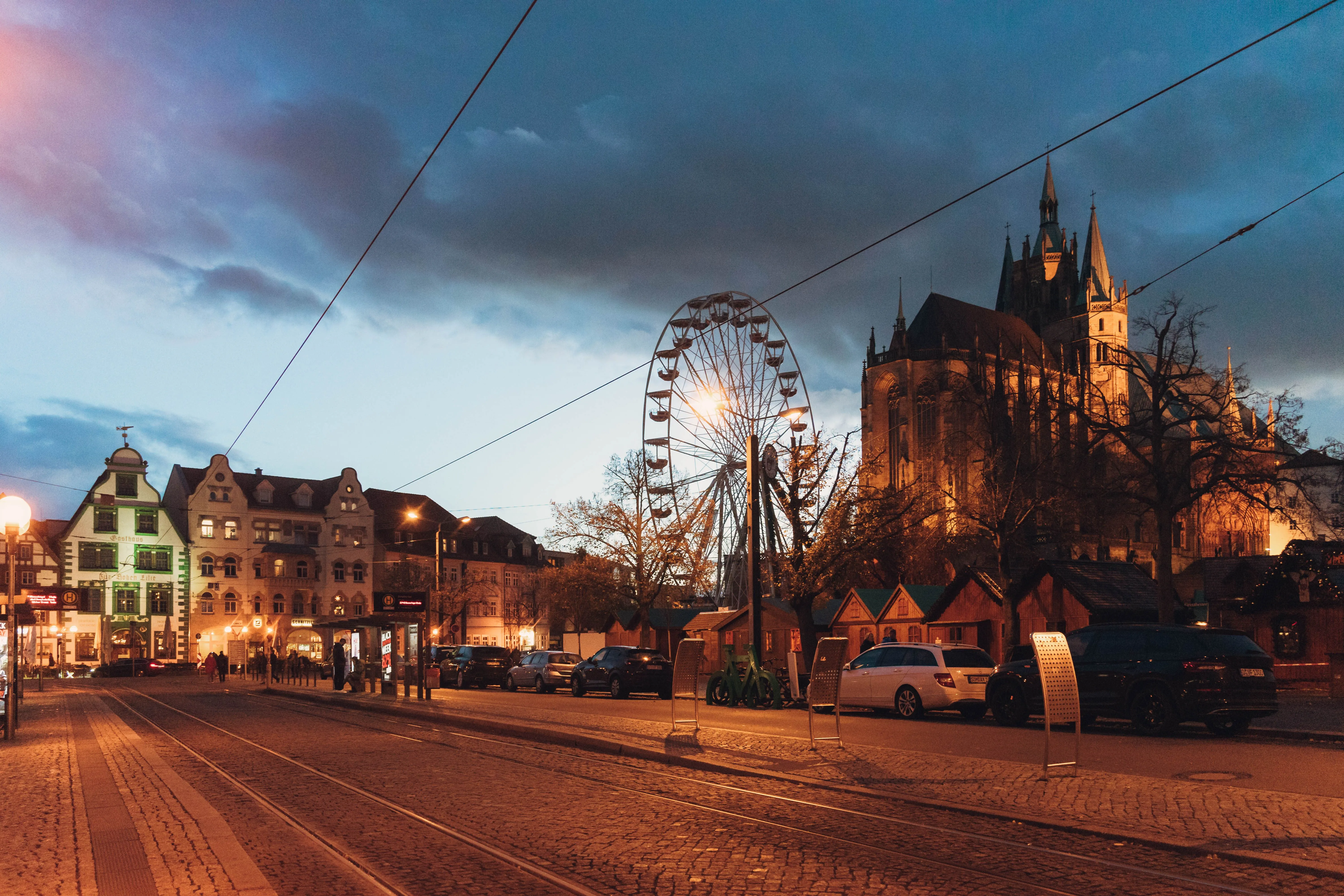 Erfurter Dom und Riesenrad bei Abenddämmerung, gesehen von einer Altstadtstraße mit Straßenbahngleisen.