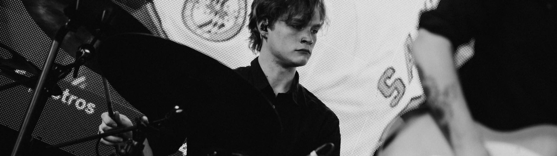 Black and white photo of a focused drummer playing a drum set during a live performance.