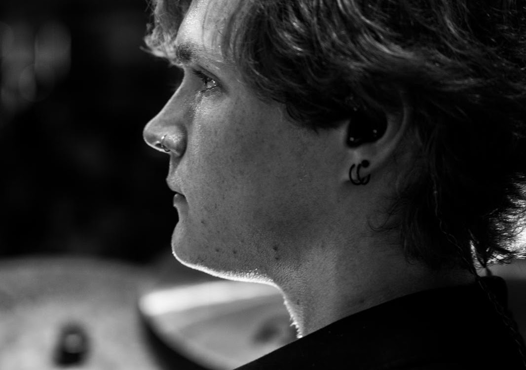 Black and white close-up profile of a person with curly hair, a nose ring, and double earrings wearing an earbud.