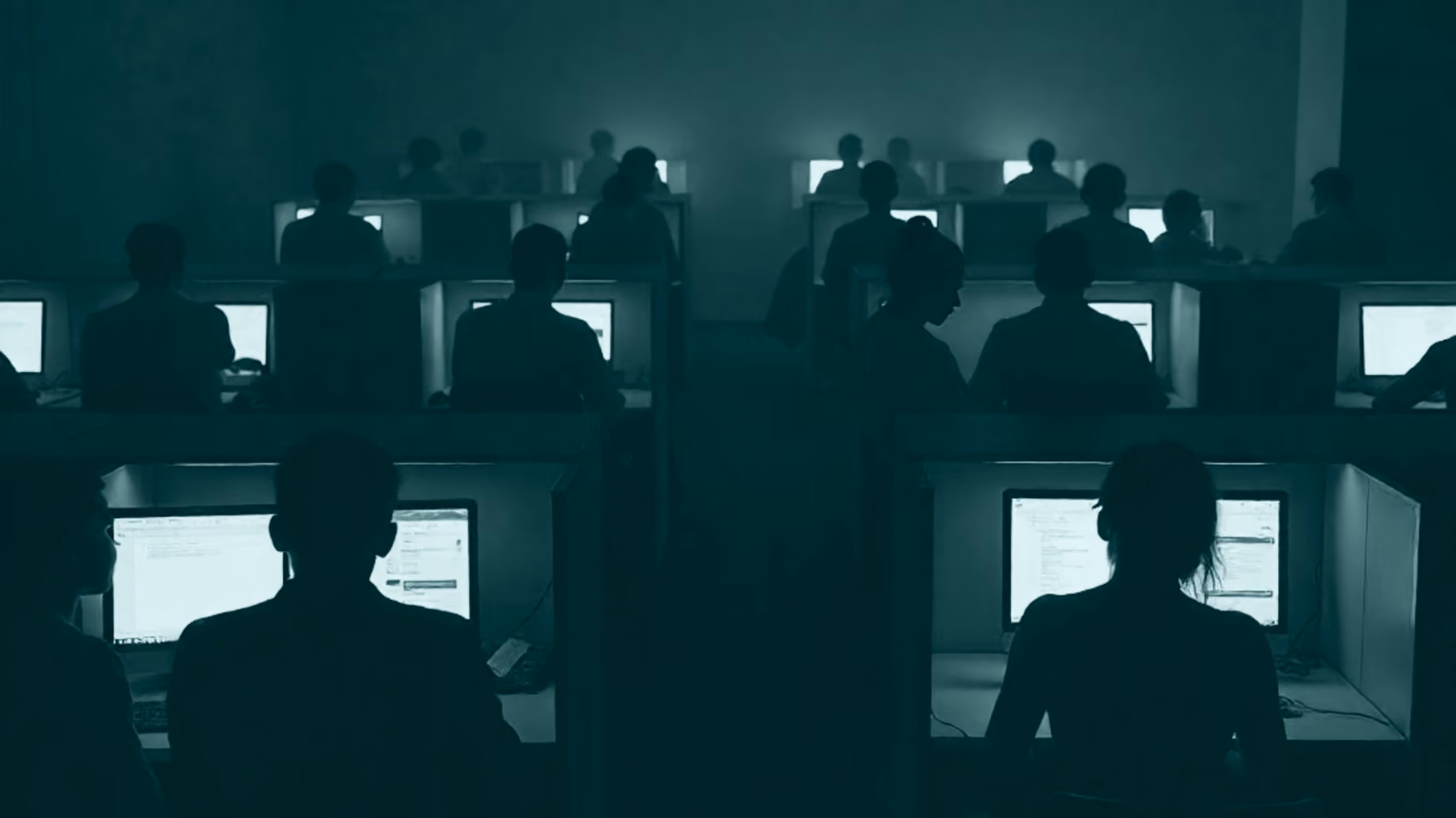 Rows of anonymous silhouettes at desks in a dark compound