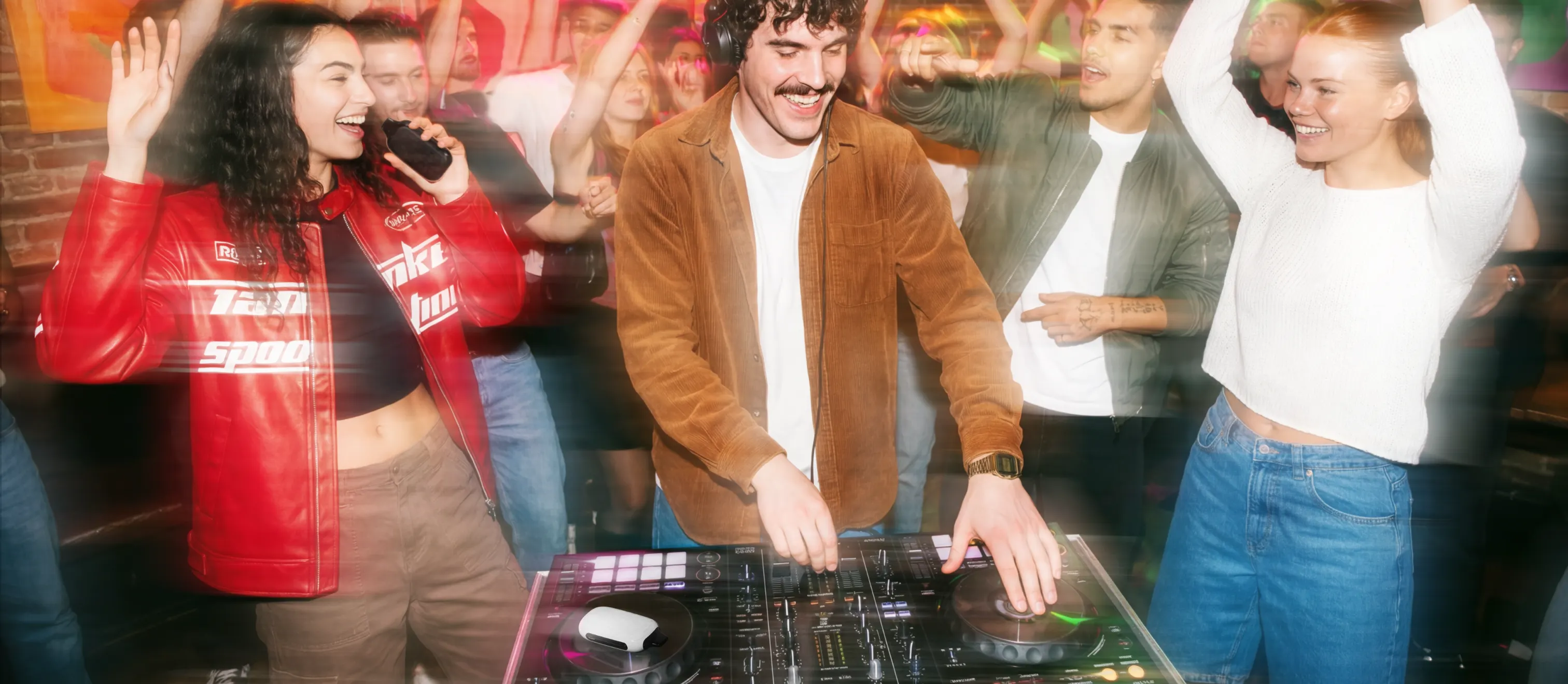 Диджей играет на пульте, окружён танцующими людьми, электронная сигарета ROQY лежит рядом с пультом