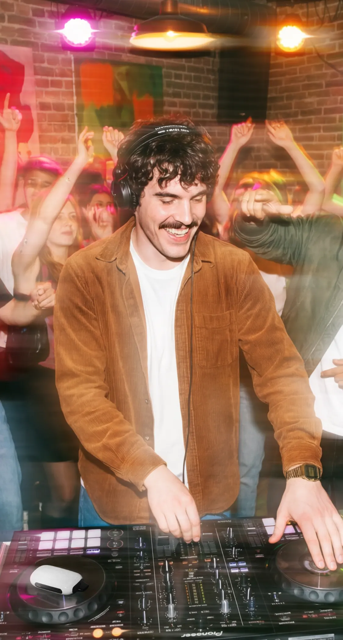 Диджей играет на пульте, окружён танцующими людьми, электронная сигарета ROQY лежит рядом с пультом