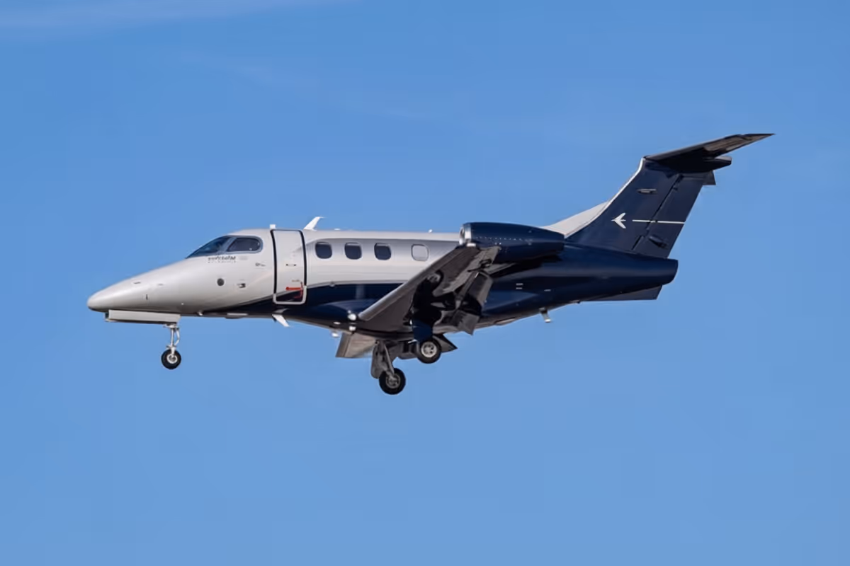 Small private jet airplane flying with landing gear extended against a clear blue sky.
