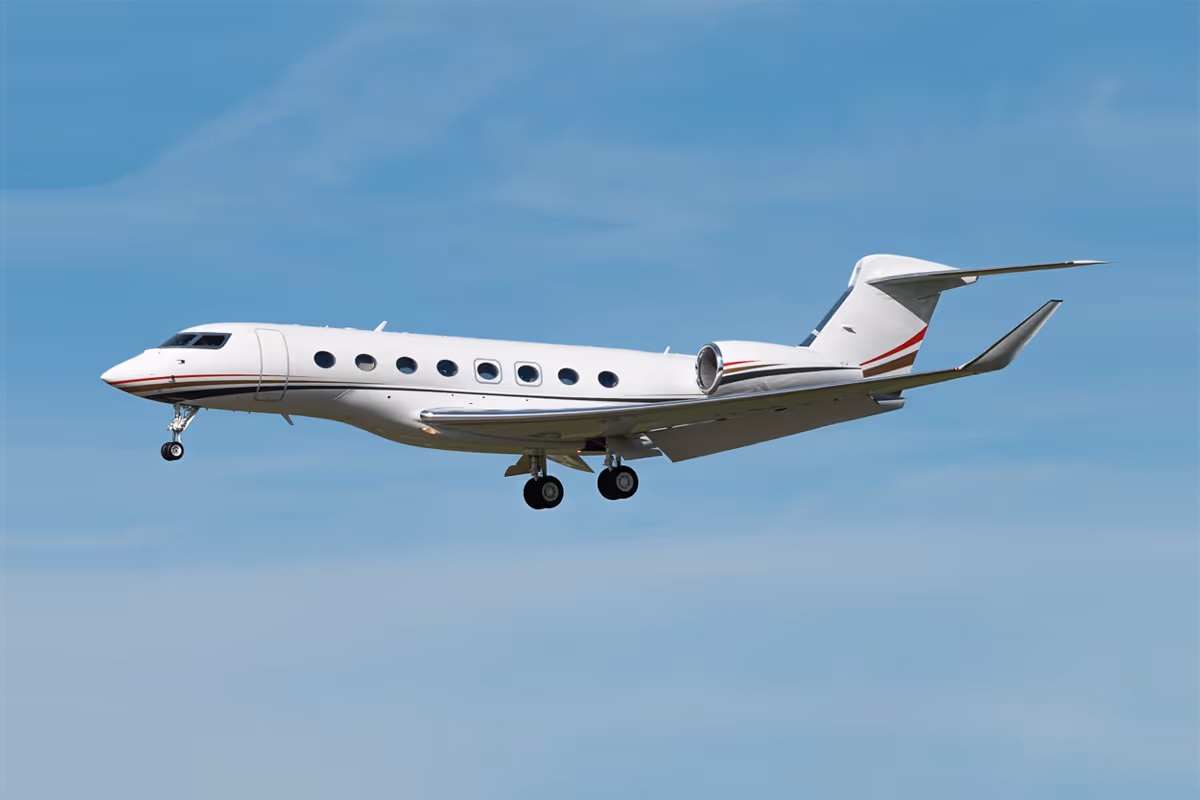 White private jet with engines mounted at the rear flying against a clear blue sky.
