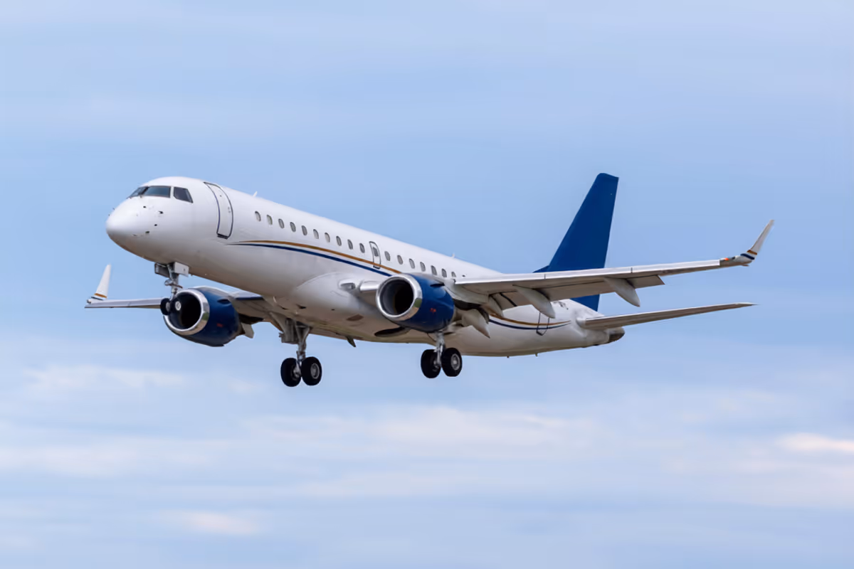 White commercial airplane with blue accents flying in a partly cloudy sky.