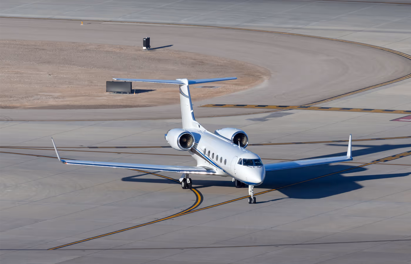 White private jet taxiing on the airport runway under clear daylight.