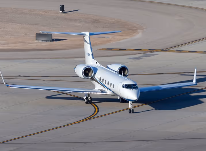 White private jet taxiing on the airport runway under clear daylight.