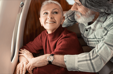 Older couple smiling and embracing each other while looking out of an airplane window.