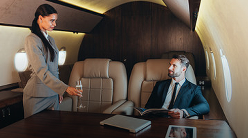 A flight attendant serving a drink to a man seated in a luxurious private jet cabin.