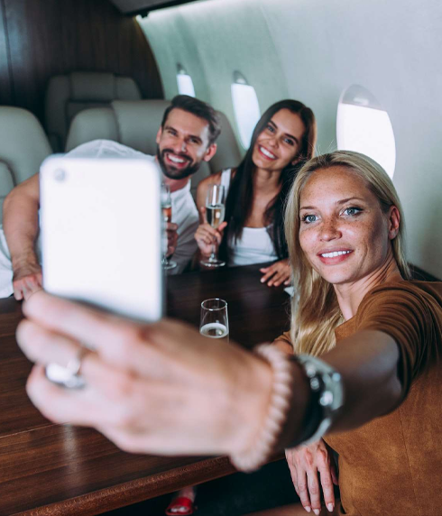Three friends smiling and taking a selfie together inside a private jet, holding glasses of champagne.