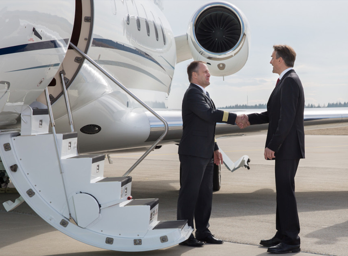 Pilot and businessman shaking hands beside a private jet on an airport tarmac.