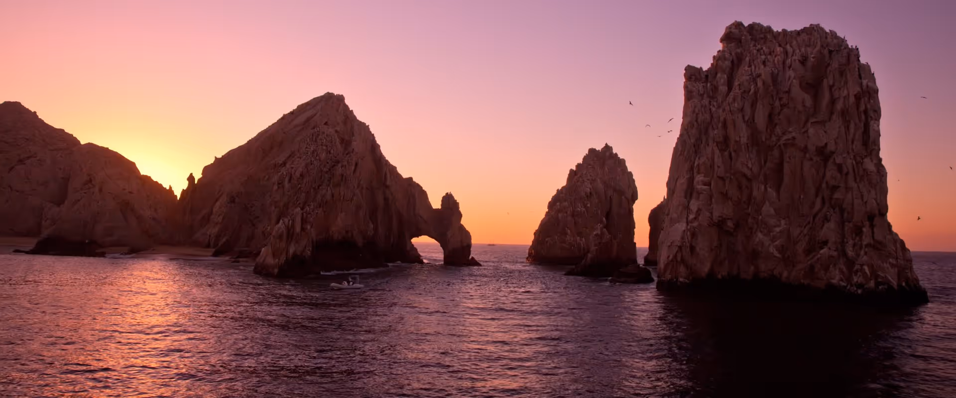 Rock formations rising from the ocean at sunset with a natural arch in the largest rock.