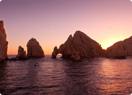Rock formations rising from the ocean at sunset with a natural arch in the largest rock.