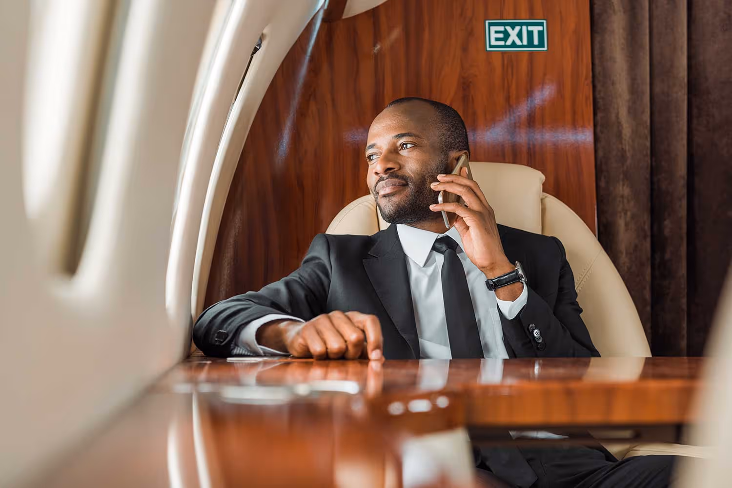 Man in a suit sitting in a private jet talking on a smartphone and looking out the window.