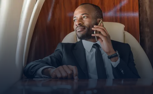 Man in a suit sitting in a private jet talking on a smartphone and looking out the window.