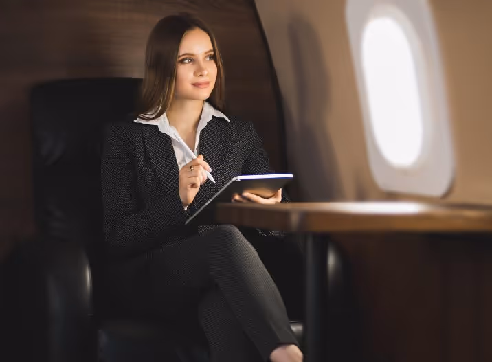 Businesswoman in a suit sitting on a leather chair inside an airplane, writing on a digital tablet.