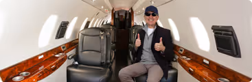 A man sitting in the aisle of an airplane giving a thumbs up.