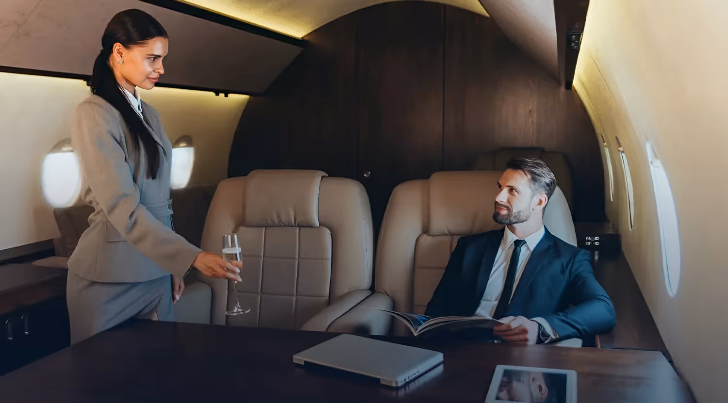 Flight attendant offering a glass of champagne to a man in a suit seated inside a private jet.