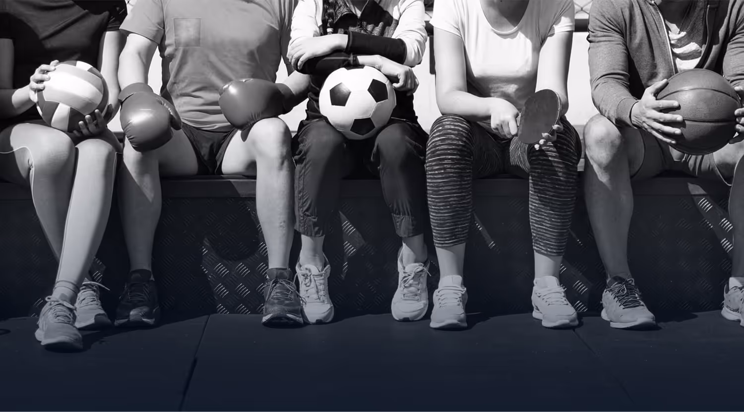 Five people sitting side by side holding different sports equipment including a volleyball, boxing gloves, soccer ball, table tennis paddle, and basketball.