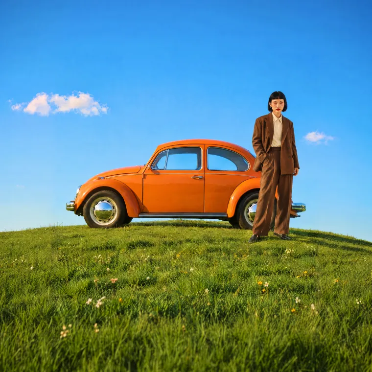 Man standing next to an orange Beetle car on a grassy hill